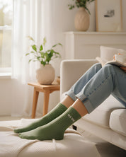 Cozy indoor lifestyle shot of a model relaxing on a couch, styling the almond green glitter message socks with casual home attire.