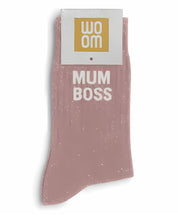 Rose gold glitter message socks with a white jacquard MUM BOSS inscription at the ankle, presented in their original Woom paper packaging.