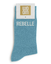 Vibrant turquoise glitter message socks with a white jacquard REBELLE inscription at the ankle, presented in their original Woom paper packaging.