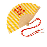 Close-up view of the opened yellow and white striped wooden fan, highlighting the crisp fabric texture, red typography, and attached contrast shoulder cord.