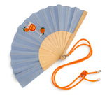 Close-up view of the opened blue wooden fan, showcasing the detailed cocktail graphics, fine fabric texture, and attached orange contrast cord.