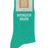 Almond green glitter message socks with a white jacquard WONDER MUM inscription at the ankle, presented in their original Woom paper packaging.